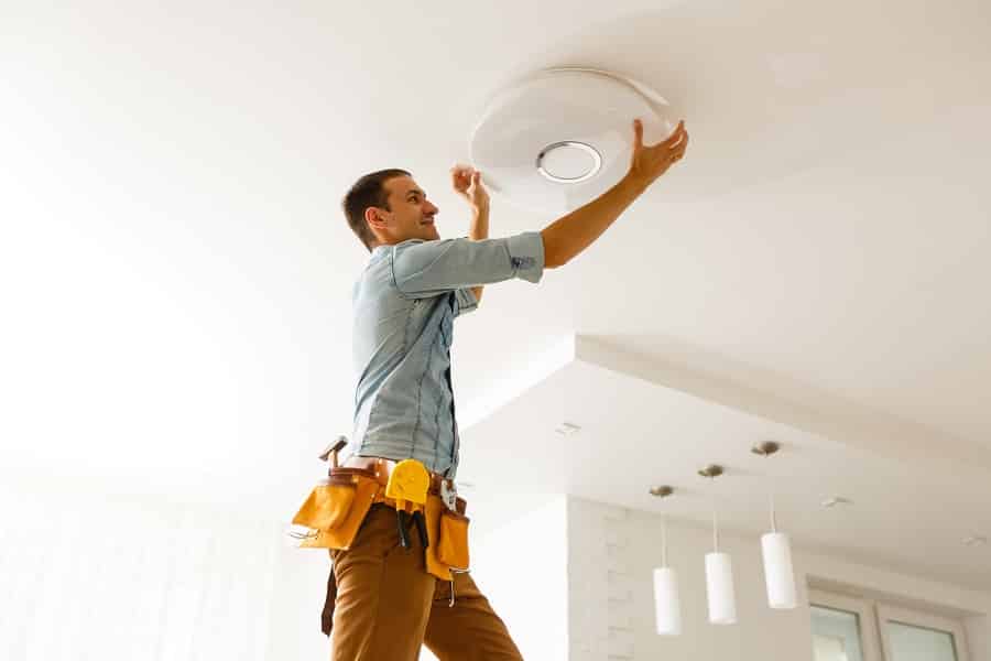 Best Electrician in Palm Beach Electrician is installing and connecting a lamp to a ceiling.