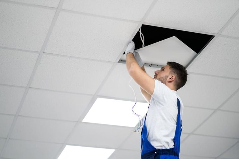 Electrician On Stepladder Installs Lighting To The Ceiling