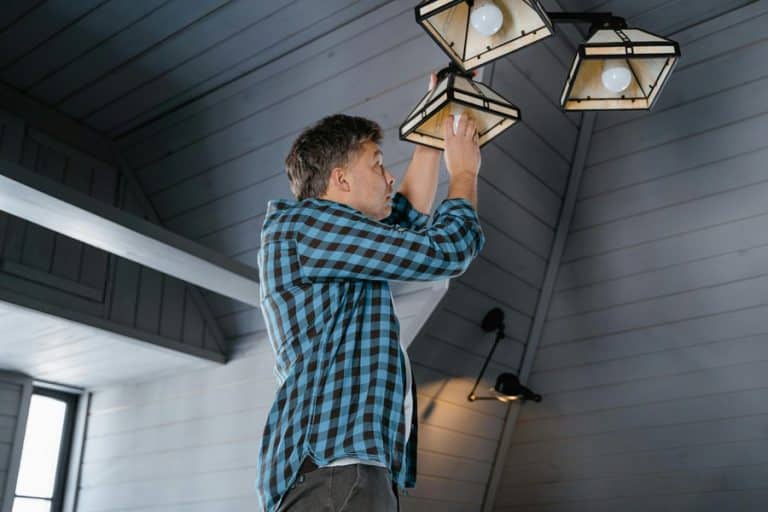Best HOA Electrician in Delray Beach An Electrician on a Ladder Installing a Pendant Light on the Ceiling of a Porch