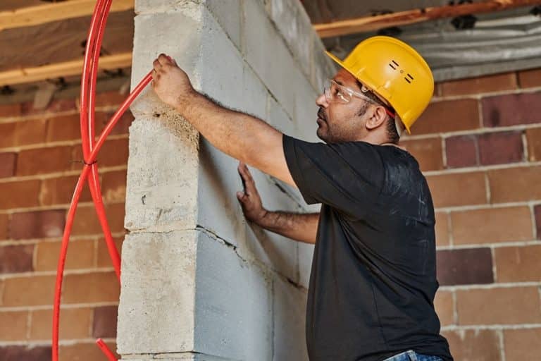 Best Electrical Contractor Serving Manalapan an Electrician Holding Up Conduit to a Brick Wall While Standing on a Ladder