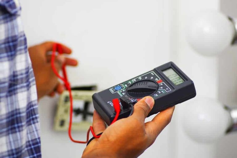 Best Electrician to Install a New Outlet in Palm Beach Gardens Man wearing white and blue shirt working on electrical wall socket wires using multimeter, electrician concept.